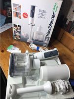Boxed Braun hand blender set with molded plastic interior packaging including hand blender, chopping bowl with blade, blending stick and measuring cup.