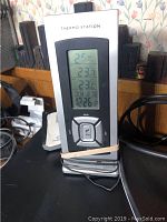 Digital Thermo Station device showing temperature readings, black and silver with buttons on front.