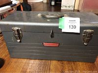 Closed gray metal Craftsman toolbox with handle and two latches, showing some wear and scratches.