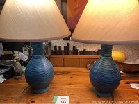 Two matching blue ceramic table lamps with beige fabric shades placed on a wooden surface.