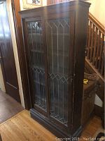 Front view showing cabinet with two leaded glass doors, wood finish and overall form