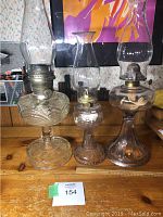 Full view of three vintage glass oil lamps of different sizes on wooden surface.