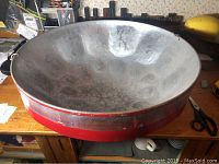 Full view of the steel drum from an angle showing the interior playing surface and part of the red exterior rim.