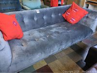 Front angle of gray tufted sofa showing seat and back cushions with two red pillows.