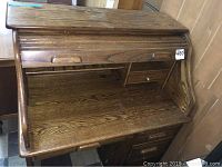 Front view of the wood roll top desk showing the roll top partially open revealing small drawers and cubbies inside.