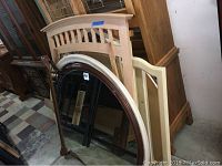 Photo showing multiple dresser mirrors including a large curved wooden frame mirror and other assorted frames leaning against furniture