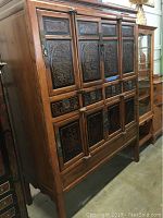 Left side angled view of vintage Asian inspired wooden cabinet showing carved panels and doors.