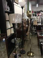 Overview of lamps and lampshades stacked on shelves and placed on floor and furniture, showing variety of styles and lampshade counts.