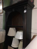 Full view of HOOKER Furniture black wooden bookshelf showing decorative top molding, fluted side columns, and arched open front with shelf. Several lamp shades are placed inside but not included.