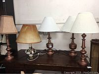Five table lamps of varying styles and shades arranged on a wooden surface, showing the lot contents.