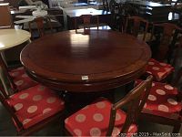 Photo of round vintage rosewood dining table with 8 matching chairs upholstered in red with white circles.