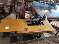 Wood cabinet with fold-out extension holding the sewing machine, showing the overall setup in an indoor setting with chairs and tables around.