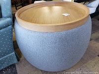 Round gray patterned fabric ottoman with a removable wooden tray top placed on it, showing the side and top view.