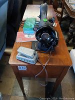 Full view of the sewing machine placed on a wooden table showing foot pedal and manual on the table beside it.