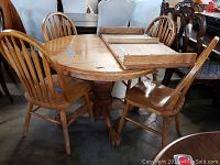 Claw foot oak round table with four oak chairs, showing the table partially extended with the leaf rack on top.