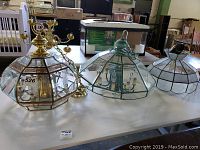 Four used hanging glass panel light fixtures displayed on a white table, varying in size and design.