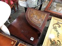 Vintage wooden corner table with elevated riser showing leather inset top with decorative border, visibly worn surface.