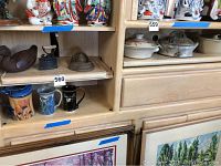 Overview of upper shelves with ceramic terrines and other stoneware pieces, along with lower shelf mugs and iron