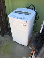 Full view of white Haier portable washing machine with coiled black hose, showing overall appliance condition and design.