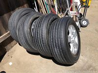 Four Bridgestone tires mounted on wheels with visible tread, positioned upright and leaning against a fence outdoors.