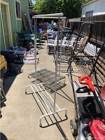 Pair of white metal clothing racks on wheels shown outdoors, highlighting frame, wheels, and shelf below hanging bar.