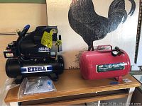 Excell air compressor and MVP red air tank side by side on wooden table.