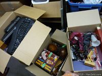 View of three open boxes containing various household items including computer keyboards, decorative objects, poker chip set, cords and brushes.