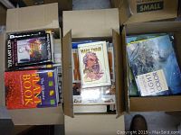 Top view of three open cardboard boxes filled with books showing some visible titles.