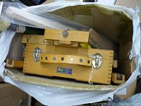 View of wooden folding artists easel inside packaging, showing leather handle and metal clasps with brand label visible.