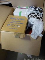 Open cardboard box with a Royal Albert bone china 3 tier cake stand box visible inside. Other wrapped items in black and white polka dot tissue paper are also present.