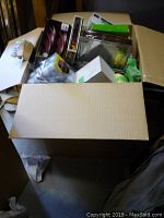 Photo showing a large cardboard box filled with assorted household items including shoehorns, boxes, and packages.