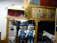 Full view of the wooden shelving holding boxed holiday light decoration and two plush snowman figures dressed in blue and white.