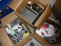 Three cardboard boxes with assorted household and kitchen items including a metal toaster oven and ceramic containers with flowers.