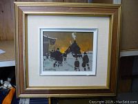 Framed painting of figures at a train station under evening sky, beige linen mat, gold wood frame