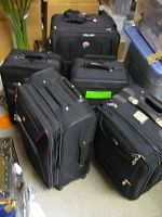 Five black suitcases of varying sizes grouped together, displaying external appearance and condition.