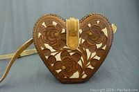 Front view of heart shaped leather purse with carved floral design and clasp closure.