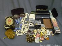 Overview of the lot showing various costume jewelry, eyeglasses with cases, a vintage floral tin, and a small velvet pouch.