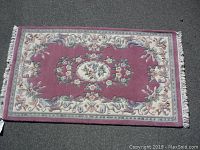 Top-down, full view of rectangular carpet showing central floral medallion pattern and fringed edges.