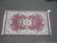 Full view of rectangular floral patterned carpet laid flat on pavement, showing design and fringes