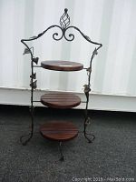 Front three-quarter view showing wooden shelves and decorative metal frame with leaf accents and scroll details.