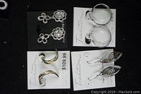 Photo showing four pairs of sterling silver earrings on black and white cards. Includes floral designs with stones, gold-tone curved pair, and filigree shaped pair.