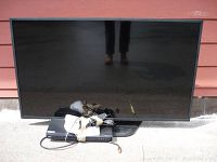 Front view of 55" LG TV on stand with Blu-ray player and bundled cables on ground