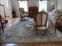 Photograph showing one of the two large floral area rugs in a living room setting beneath chairs and a small table, showing size and design.