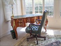 Full view of the leather top legal desk with gilded brass edges and wooden arm rolling chair in front.
