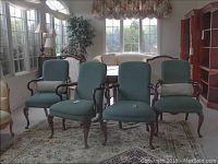 Four matching upholstered armchairs arranged in a living room, green fabric seats and backs with wooden armrests and legs, visible wear on wood
