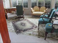 Photo showing both rugs in a sunlit conservatory with furniture around, depicting the larger beige-green rug with the smaller medallion rug on top.