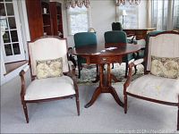 View of two matching upholstered accent chairs with carved wood frames and decorative pillows, placed beside a wooden round table in a room with carpet flooring.