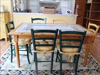View of full set showing rectangular wooden table with floral tile top surrounded by six chairs in green and yellow colors, with cushions on green chairs.