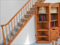Full view of the wood corner shelf unit positioned next to staircase, showing its height and multiple shelves.