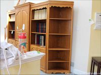 Wooden corner shelf next to matching furniture pieces with books inside adjacent shelves. Shelf is empty with visible scalloped trim detail.